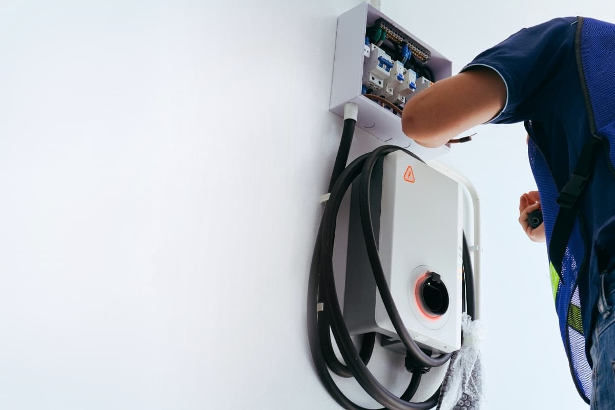 A technician installing a wall-mounted EV charger beside an open electrical sub-panel